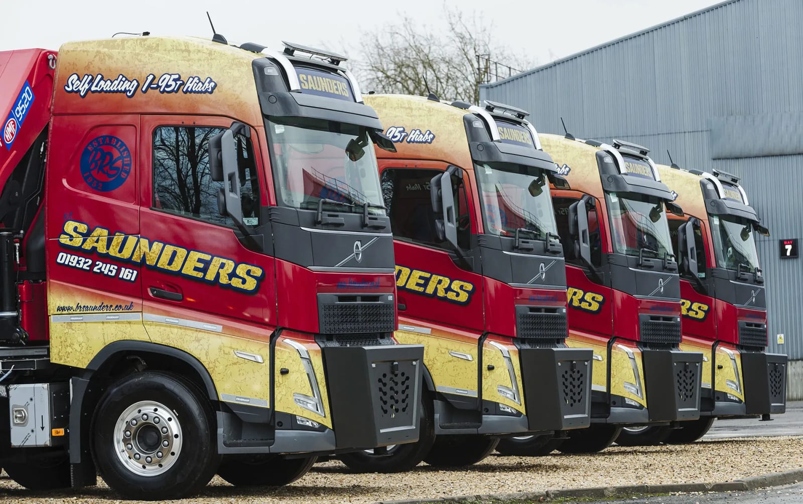 Five red and yellow BR Saunders Transport Volvo lorries fitted with lorry-mounted cranes, parked in a row outside a depot